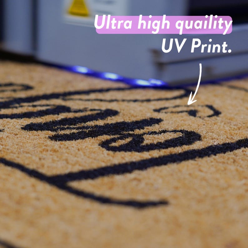 Puede incluir: Primer plano de una alfombra de coco marr&oacute;n con letras negras que dicen "Hello". La alfombra est&aacute; iluminada por una tira de luz LED azul. El texto "Ultra high quality UV Print." es visible en el fondo.