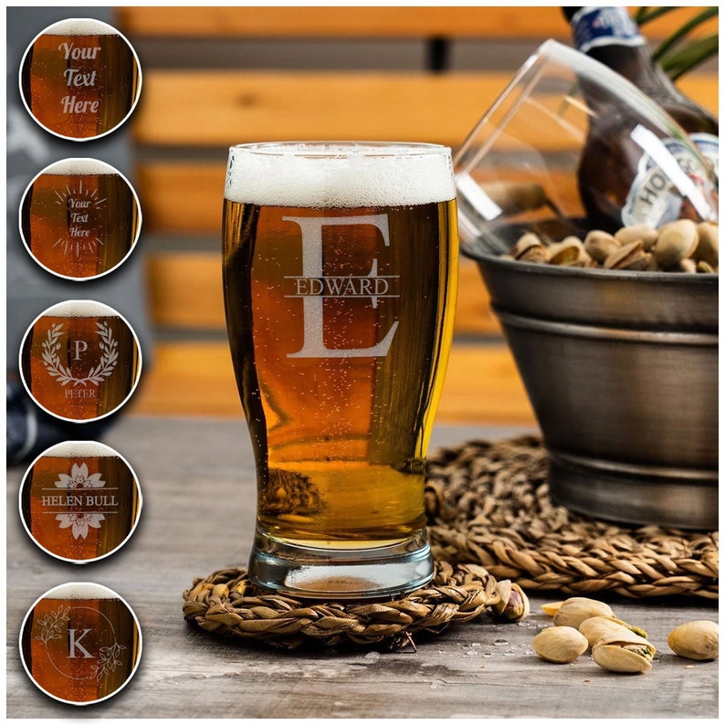 May include: A personalized beer glass with the name "EDWARD" etched on the side. The glass is filled with a golden-colored beer and is sitting on a woven coaster. There are pistachios scattered on a wooden surface.