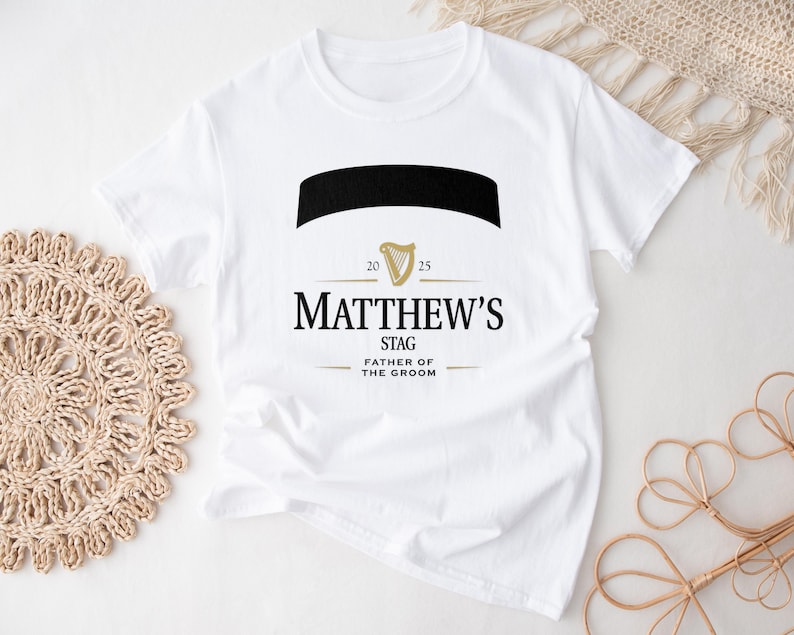 May include: White t-shirt with a black and gold design. The design includes the name "Matthew's", the word "Stag", and "Father of the Groom". The design also features a black banner and a gold harp symbol.