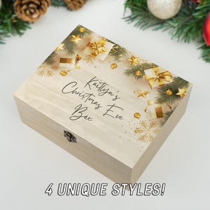 Puede incluir: Una caja de madera con un diseño navideño dorado y verde. La caja está decorada con estrellas doradas, copos de nieve y regalos. El texto en la caja dice "Kaitlynn's Christmas Eve Box".