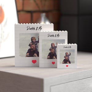 Set of three customizable photo blocks made from white building bricks, each featuring a cherished "Daddy & Me" image and elegant black script, accented by a bright red heart. Available in three different sizes, this charming collection is perfect as a meaningful Father's Day gift or personalized home decor keepsake.