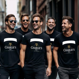 May include: Five men wearing black t-shirts with the text "Charlie's Stag" and a white banner. The shirts also feature the text "The Best Man", "The Groom", and "The Groomsman". The men are smiling and wearing sunglasses.