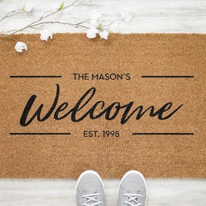May include: A brown coir doormat with the text "The Mason's Welcome Est. 1998" in black lettering.