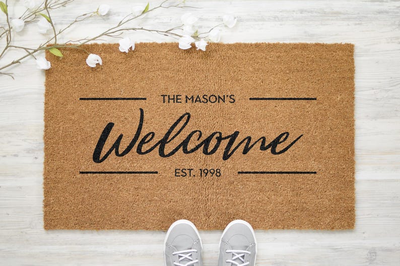May include: A brown coir doormat with the text "The Mason's Welcome Est. 1998" in black lettering.