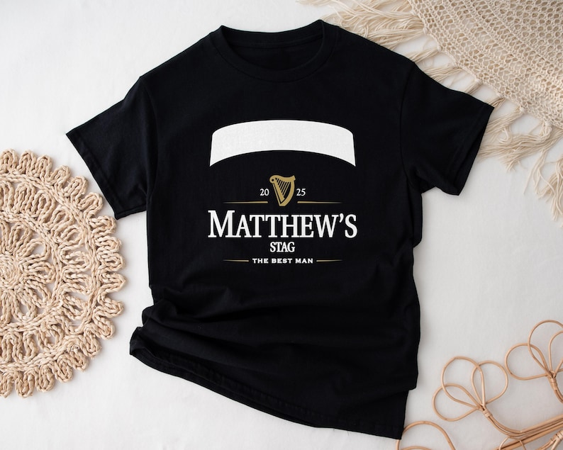May include: Black t-shirt with a white banner and gold harp graphic. The text reads "Matthew's Stag" with "The Best Man" below. The shirt also has the numbers "20" and "25" on the design.