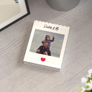 Personalized photo block made of white building bricks, featuring a printed image of a father carrying his child on his shoulders, captioned "Daddy & Me" in elegant script, accented by a vibrant red heart. Ideal as a heartfelt, custom gift for Father's Day or family celebrations.