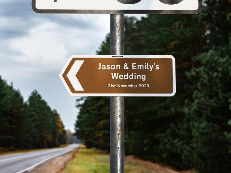 May include: A brown and white directional sign with an arrow pointing left. The sign reads "Jason & Emily's Wedding 21st November 2023".