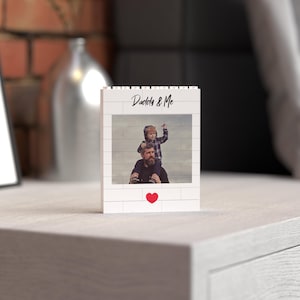 Personalized standing photo block crafted from white building bricks, showcasing a custom printed photo of a father and child moment, labeled "Daddy & Me" in stylish text, and finished with a charming red heart detail. Perfect as a unique and sentimental Father's Day gift or home decor keepsake.