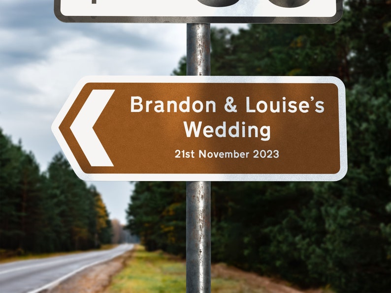 May include: A brown and white directional sign with a white arrow pointing left. The sign reads "Brandon & Louise's Wedding 21st November 2023".