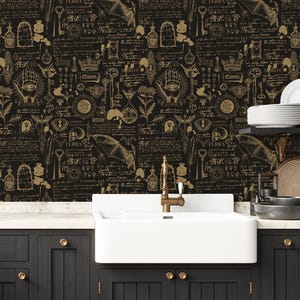 May include: Wallpaper featuring a repeating pattern of gold-colored occult and botanical illustrations on a black background. The design includes drawings of bats, keys, hands with eyes, hourglasses, crowns, and handwritten script text throughout.