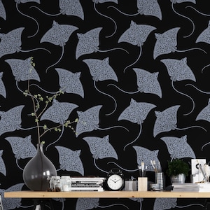 May include: Black wallpaper featuring a repeating pattern of stylized, light blue stingrays. The stingrays have a dotted texture and long, curved tails. The wallpaper is used as a backdrop for a wooden desk with various office supplies and decor.