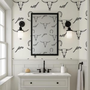 May include: A bathroom with a white vanity, black fixtures, and a mirror. The wallpaper features a repeating pattern of black bull skulls, revolvers, and horseshoes. Two black sconces flank the mirror, and a white towel hangs on a ring.