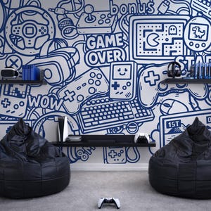 Könnte beinhalten: Ein Raum mit zwei schwarzen Sitzsäcken und einer weißen Wand, die mit einem blauen Linienmuster aus Spielkonsolen, Controllern, Tastaturen und Texten wie "GAME OVER", "bonus", "START", "wow", "1ST" und "01:23" bedeckt ist.