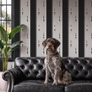 May include: A brown and white dog with a brown collar sits on a black leather couch. The background features a striped wallpaper with black, gray, and white vertical stripes. The wallpaper has a repeating pattern of small figures.