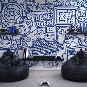 Puede incluir: Una habitación con temática de juegos con una pared blanca con arte de garabatos azules de mandos de videojuegos, consolas y frases como "GAME OVER" y "WOW". Dos pufs negros están sobre un suelo gris. Un mando blanco está en el suelo.