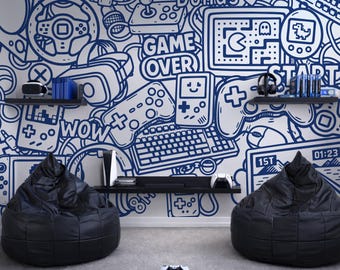 Pode incluir: Um quarto com tema de jogos com uma parede branca com arte de rabiscos azuis de controladores de videogame, consoles e frases como "GAME OVER" e "WOW". Duas cadeiras de saco pretas estão em um chão cinza. Um controlador de jogo branco está no chão.