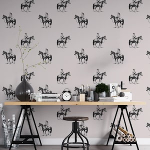 May include: Wallpaper featuring a repeating pattern of black cowboy and horse illustrations on a light gray background. The room includes a wooden desk, black metal legs, a black stool, and decorative items.