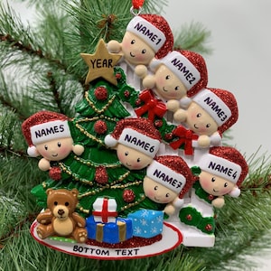 May include: A white Christmas tree ornament with six children peeking out from behind it. The children are wearing red Santa hats with white trim and have smiling faces. The tree is decorated with a gold star, red and green ornaments, and a red bow. The ornament also features a teddy bear, a blue gift box, and the text "BOTTOM TEXT".
