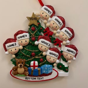 May include: A red and green Christmas tree ornament with eight children peeking out from behind a white picket fence. The ornament features a gold star, a teddy bear, and a blue gift box. The text "YEAR" is on the star and "BOTTOM TEXT" is at the bottom of the ornament.