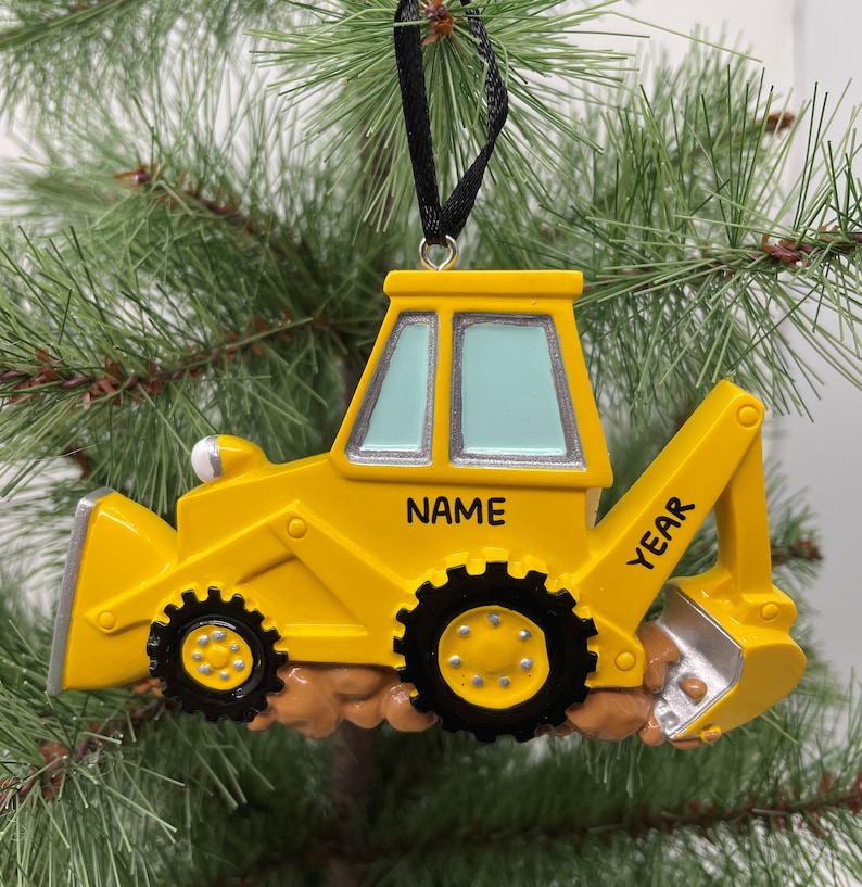 Puede incluir: Adorno de Navidad de excavadora amarilla de juguete con una cinta negra. El adorno tiene espacio para un nombre y un a&ntilde;o.