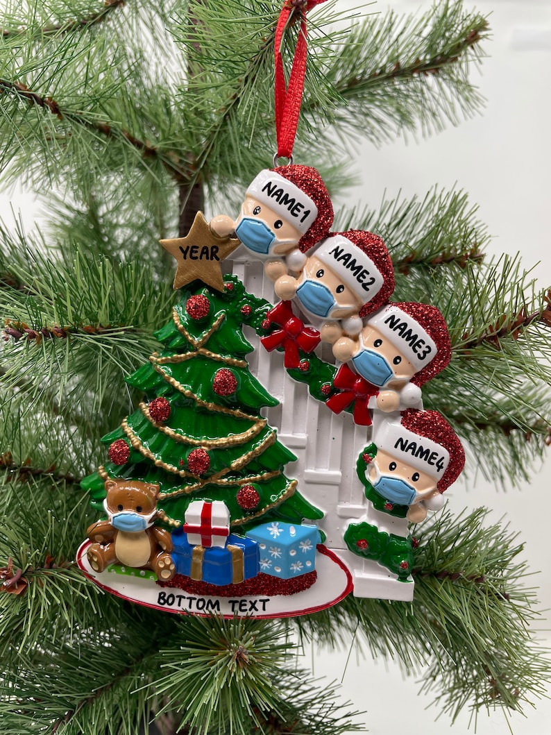 May include: A Christmas ornament featuring a family of four wearing Santa hats and face masks, decorating a Christmas tree. The ornament also includes a teddy bear wearing a face mask and a banner that says "BOTTOM TEXT".