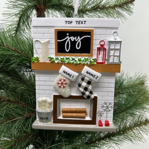 May include: White brick fireplace Christmas ornament with a chalkboard that says "joy", two stockings, a bucket of logs, and the text "NAME1", "NAME2", and "YEAR".