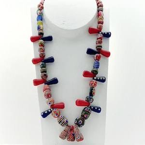 Könnte beinhalten: Eine bunte Halskette aus roten, blauen und weißen Glasperlen. Die Perlen sind auf einer Schnur aufgefädelt und haben verschiedene Muster. Die Halskette ist etwa 50 cm lang.
