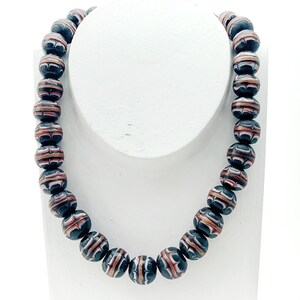 Könnte beinhalten: Eine Halskette aus schwarzen, weißen und roten Perlen mit Muster. Die Perlen sind rund und haben ein geometrisches Design.