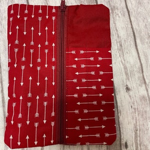 May include: A red zippered pouch with a white arrow pattern. The pouch is made of fabric and has a zipper closure.