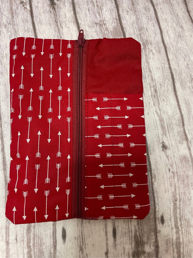 May include: A red zippered pouch with a white arrow pattern. The pouch is made of fabric and has a zipper closure.