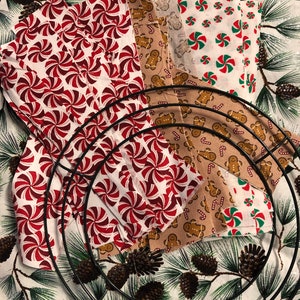 Op de afbeelding: Een verzameling stofresten met kerstthema's, waaronder pepermuntstokken, gingerbreadmen en sneeuwvlokken, gerangschikt rond een metalen kransvorm.