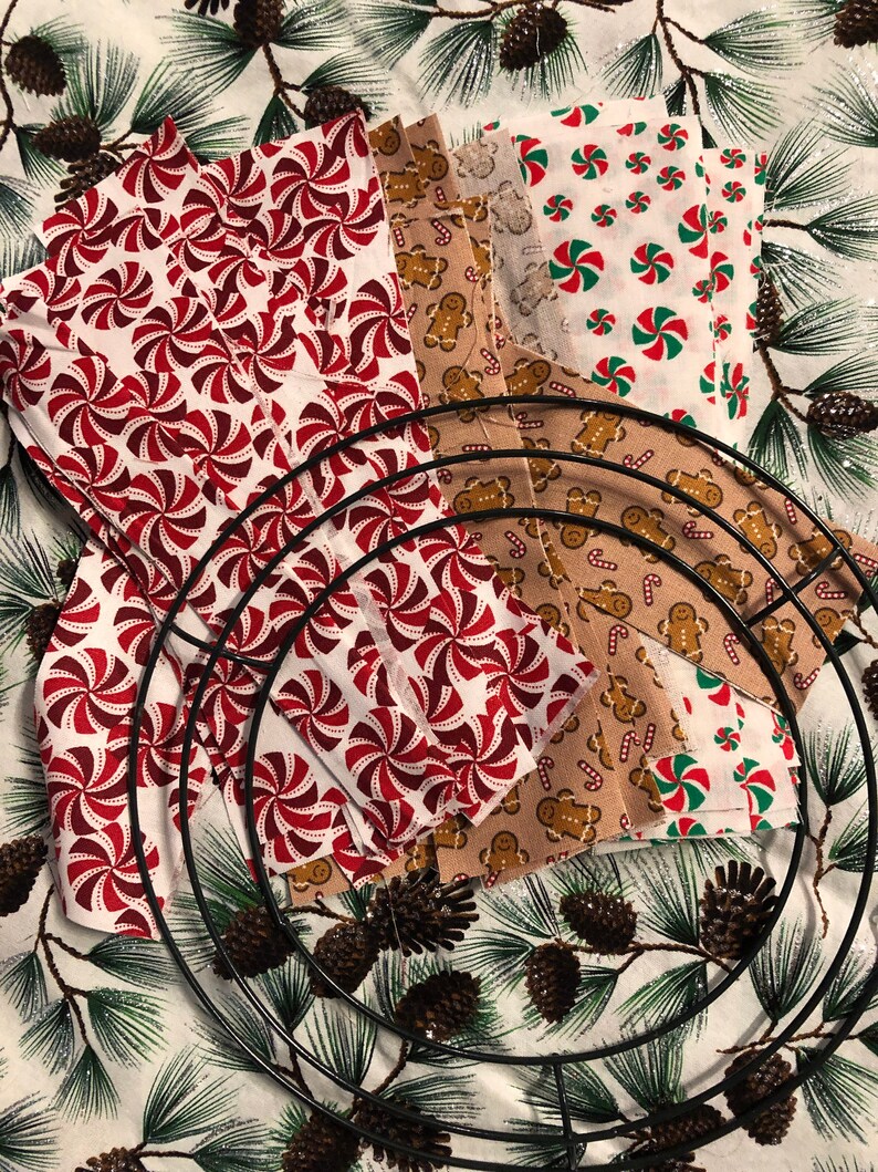 Op de afbeelding: Een verzameling stofresten met kerstthema's, waaronder pepermuntstokken, gingerbreadmen en sneeuwvlokken, gerangschikt rond een metalen kransvorm.