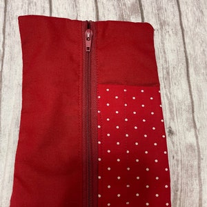 May include: A red zippered pouch with a white polka dot fabric panel on one side. The pouch is made of a soft, red fabric.