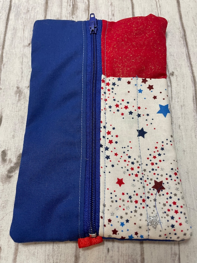 May include: A blue and red zippered pouch with a white fabric background featuring red, blue and silver stars.