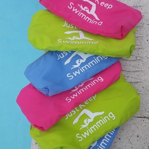 May include: A stack of six colorful drawstring bags with the text "Just Keep Swimming" and a silhouette of a swimmer on each bag.