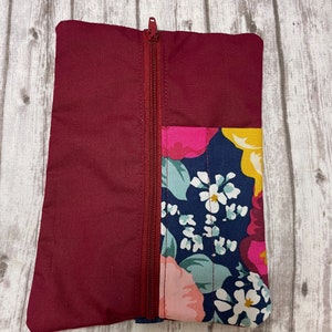 May include: A burgundy zippered pouch with a floral print on one side. The floral print features pink, yellow, and white flowers on a dark blue background.