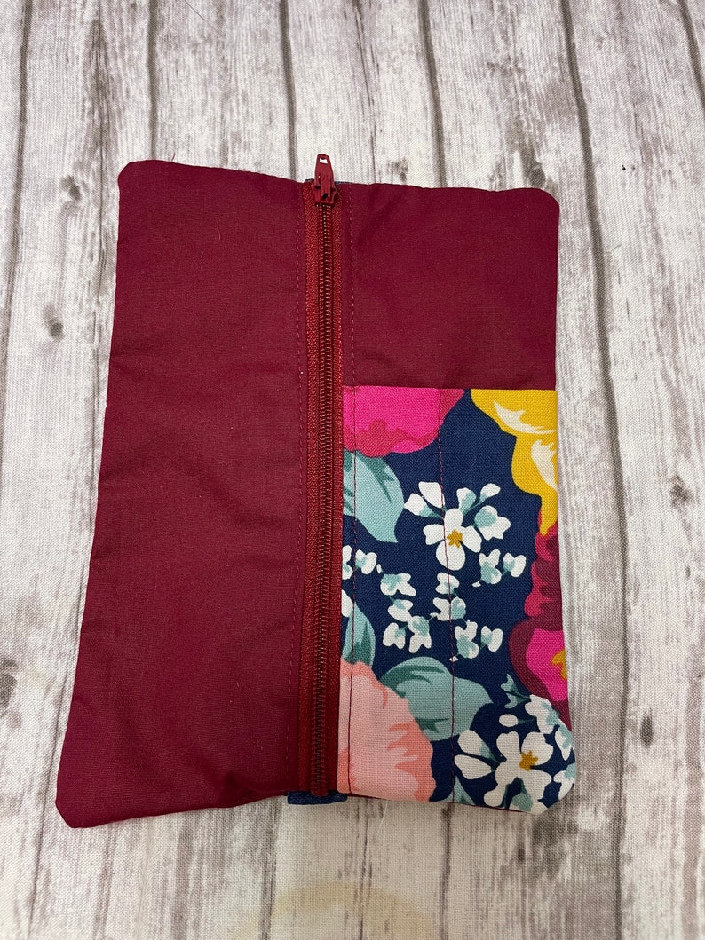 May include: A burgundy zippered pouch with a floral print on one side. The floral print features pink, yellow, and white flowers on a dark blue background.