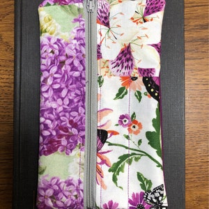 May include: A purple and white floral zippered pouch with a silver zipper and a purple zipper pull. The pouch is lying on a black surface.