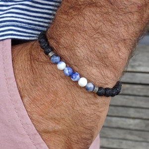 Op de afbeelding: Een kralenarmband met zwarte lavasteenkralen en een reeks blauwe, witte en blauw gespikkelde kralen. De armband is geregen op een elastisch koord en bevat zilverkleurige metalen afstandhouders.