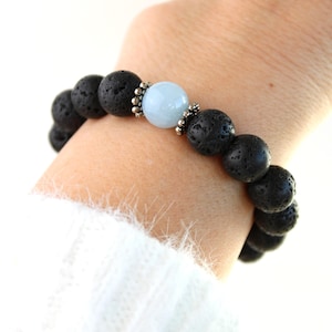 Puede incluir: Una pulsera de piedra de lava negra con una cuenta azul claro. La pulsera presenta cuentas negras redondas y porosas y una sola cuenta azul claro. Las cuentas están ensartadas con un espaciador plateado.