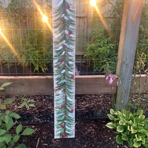 May include: A painted wooden sign featuring a green Christmas tree with red baubles. The sign is attached to a wooden fence post.