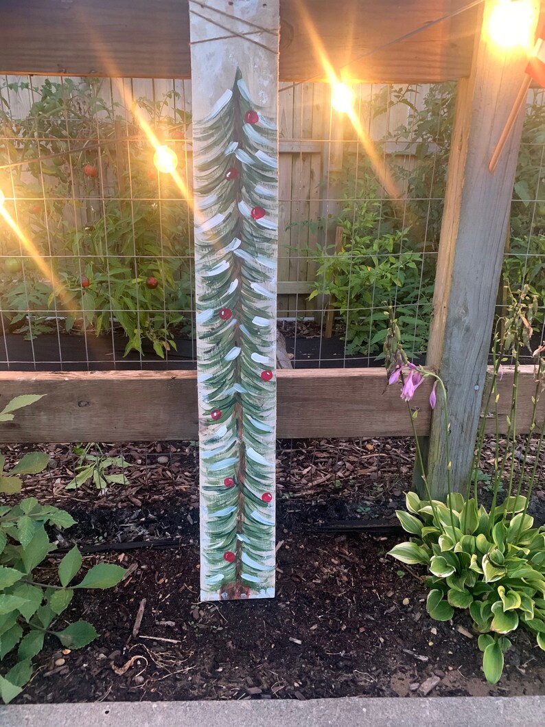 May include: A painted wooden sign featuring a green Christmas tree with red baubles. The sign is attached to a wooden fence post.