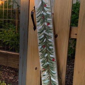 May include: A wooden plank with a painted green Christmas tree with red baubles. The tree is painted on a white background with a rustic wood texture.