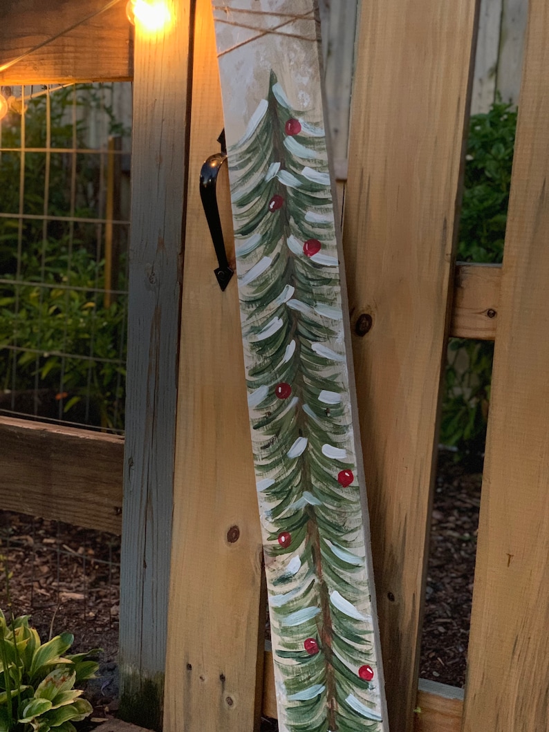 May include: A wooden plank with a painted green Christmas tree with red baubles. The tree is painted on a white background with a rustic wood texture.