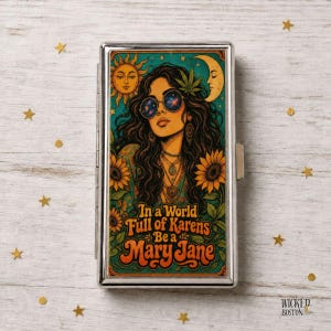May include: A rectangular metal cigarette case featuring a colorful illustration of a person with long dark hair wearing round sunglasses, surrounded by sunflowers, a sun, and a crescent moon. The text reads In a World Full of Karens Be a Mary Jane.