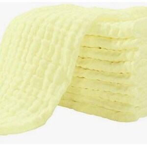 May include: A stack of pale yellow muslin cloths, folded and ready to use. The cloths are soft and absorbent, perfect for cleaning or drying.