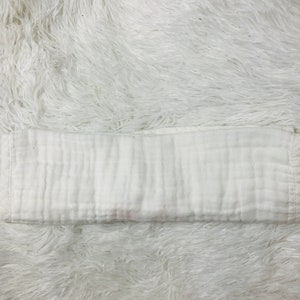 May include: A white, folded muslin cloth diaper. The diaper is made of a soft, breathable fabric and is perfect for babies.
