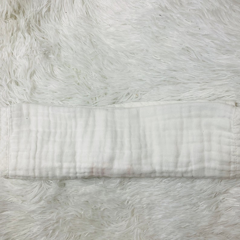 May include: A white, folded muslin cloth diaper. The diaper is made of a soft, breathable fabric and is perfect for babies.