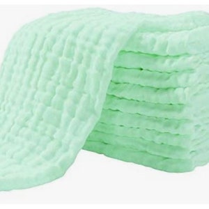 May include: A stack of light green muslin cloths, folded and arranged in a pile. The cloths are soft and textured, with a waffle-like pattern.