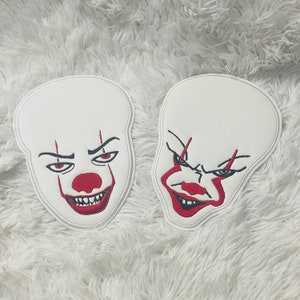 May include: Two white felt patches with embroidered images of Pennywise the clown from the movie "IT". The patches feature a red nose, red lips, and black eyes.
